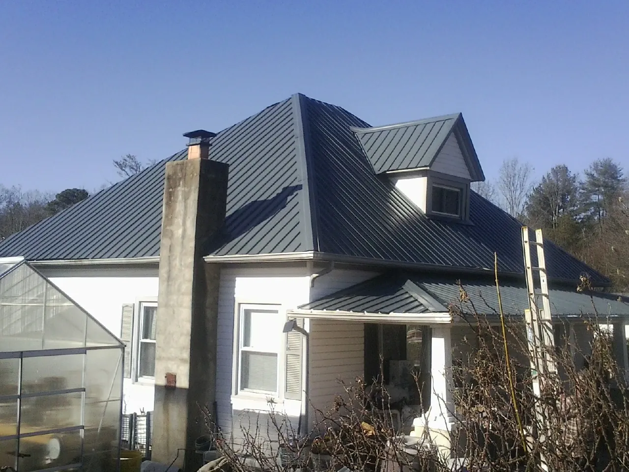 Dark blue standing seam metal roof on a white farmhouse with dormer — Slate & Tile Roof Repair by Roofing Brothers in Newell