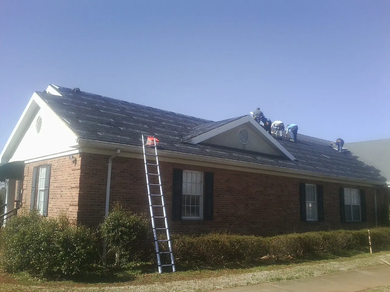 Crew tearing shingles off a brick ranch roof with a ladder set — Emergency Roof Repair work by our crew in Newell