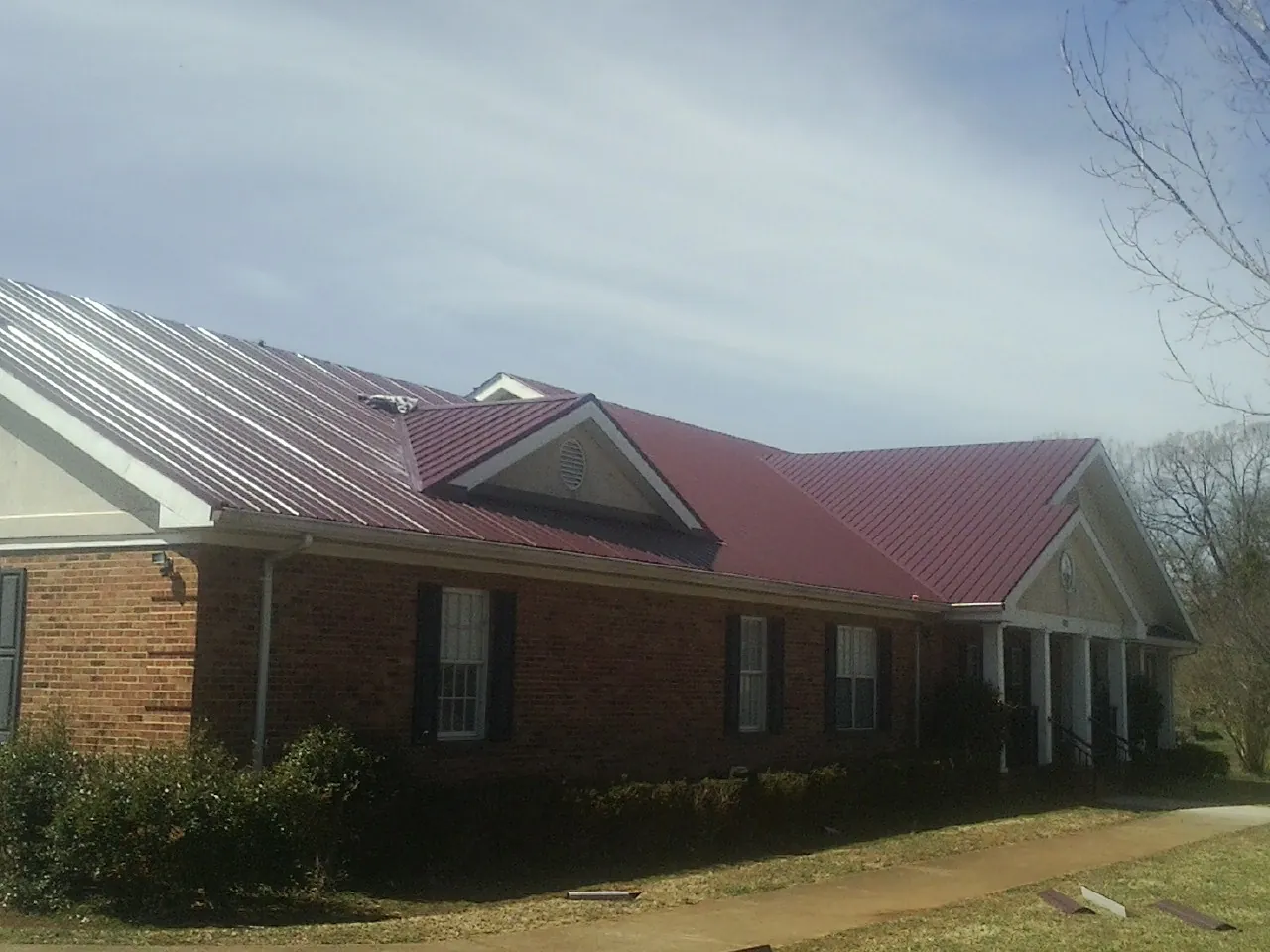 Red metal roof with gabled entries on a long brick building, from a Hail Damage Roof Repair job in Newell
