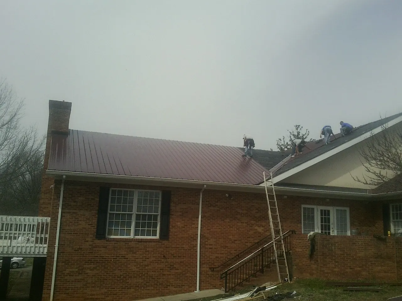 Crew setting red metal roofing panels on a brick home in Newell
