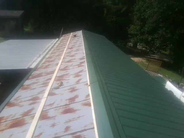 Old rusted panels beside newly installed green metal roofing — Wind Damage Roof Repair by Roofing Brothers in Newell