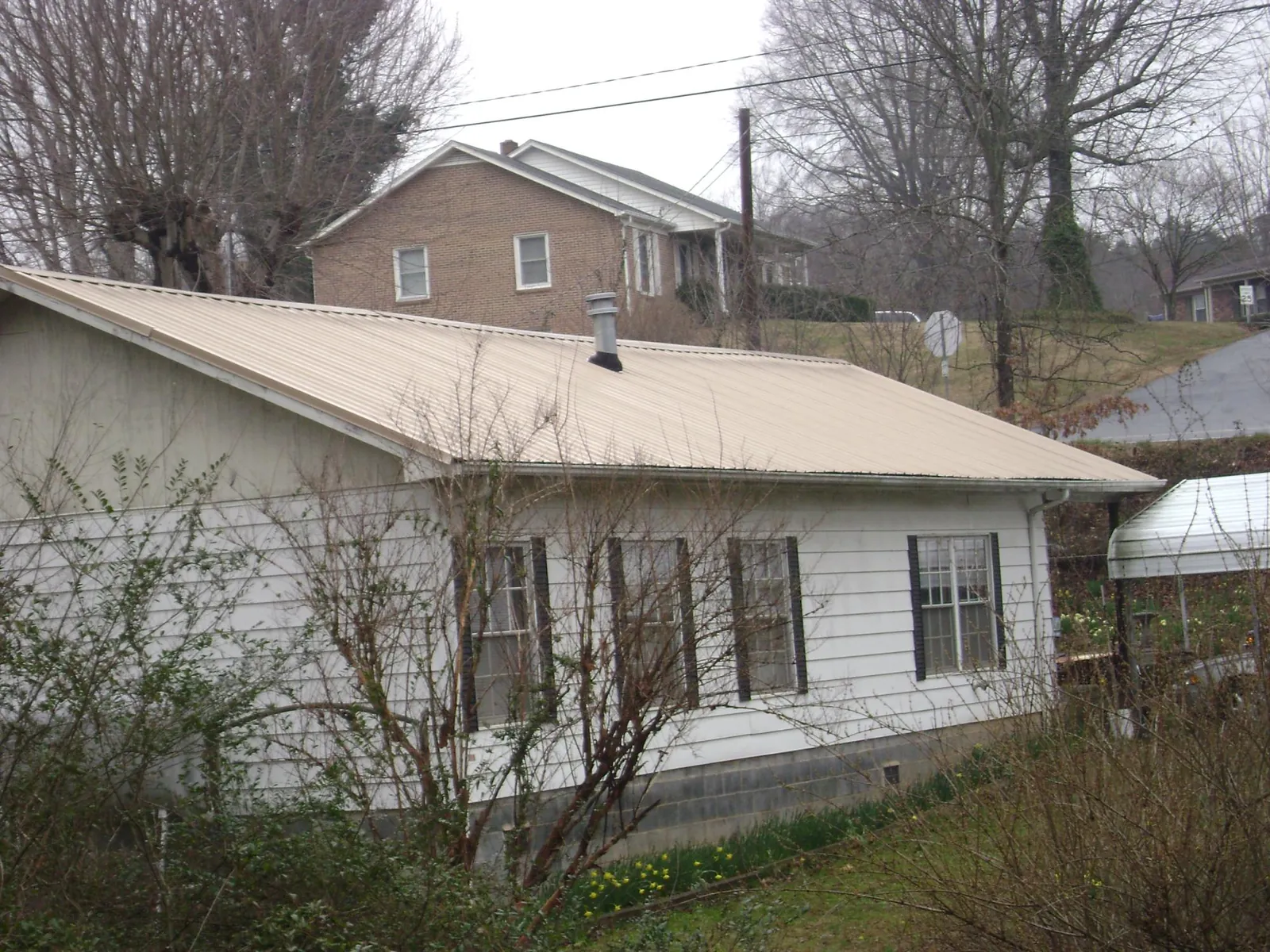 Tan metal roof on a white sided house set into a hillside — Commercial Roofing by Roofing Brothers in Newell