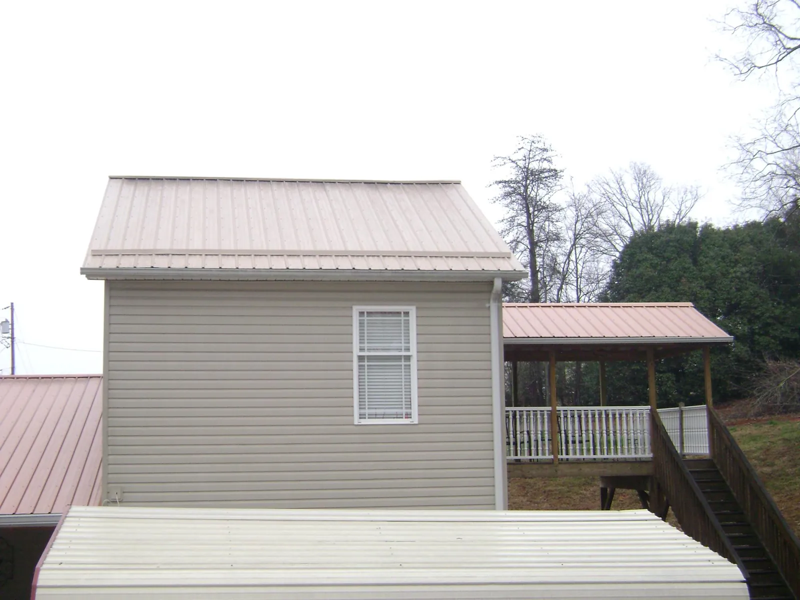 Tan metal roofs on a two story addition and attached porch, from a Roof Replacement job in Newell